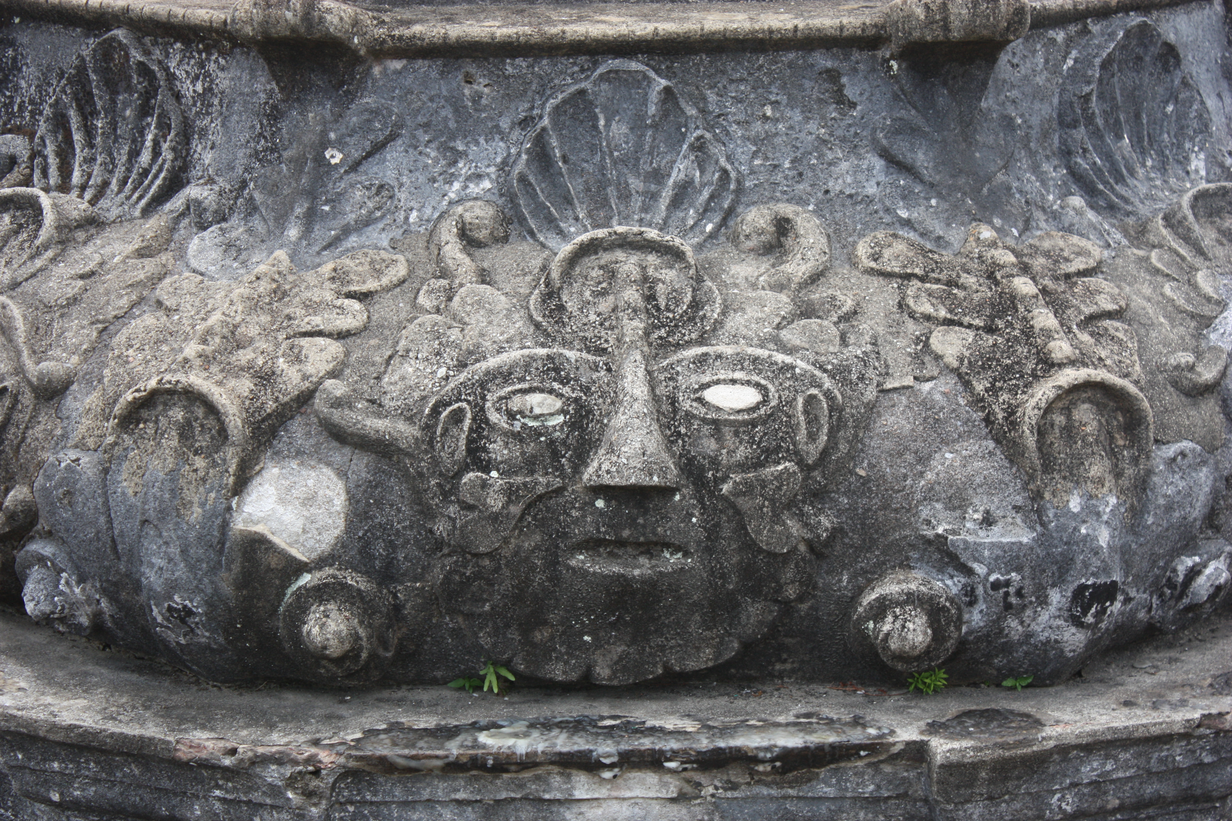 Detalhes das máscaras esculpidas em baixo relevo na base do cruziero
